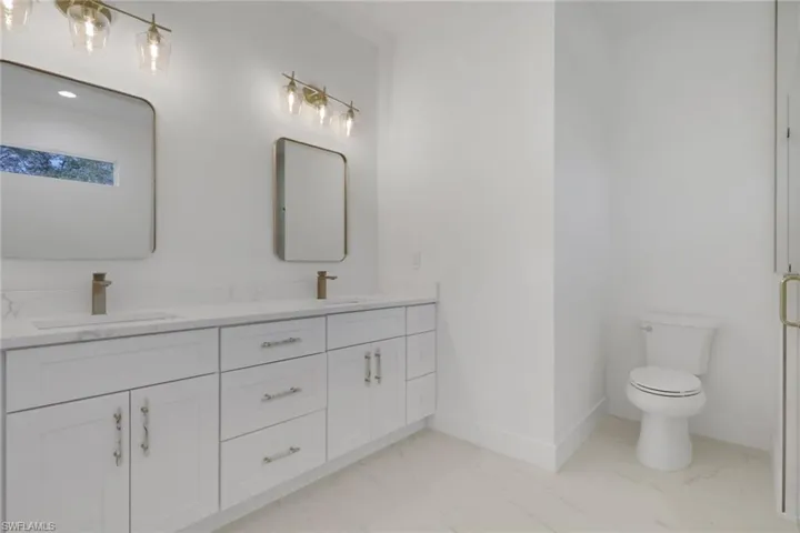 Primary bathroom featuring double vanity, light marble finish flooring, and a shower with glass door