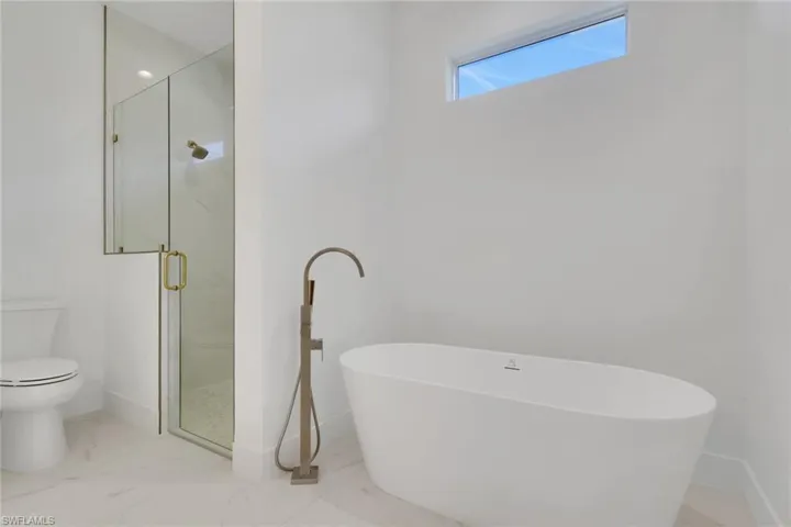 Primary bathroom featuring a shower, a freestanding tub, and light marble finish flooring