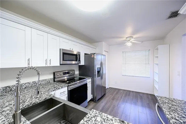 Kitchen featuring stainless steel appliances, dark wood finished floors, white cabinets, a ceiling fan, and light stone countertops