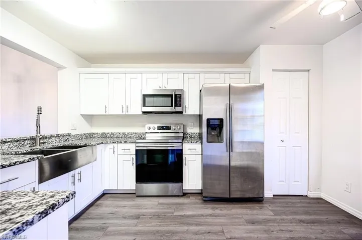 Kitchen with stainless steel appliances, dark stone counters, white cabinets, and light wood finished floors