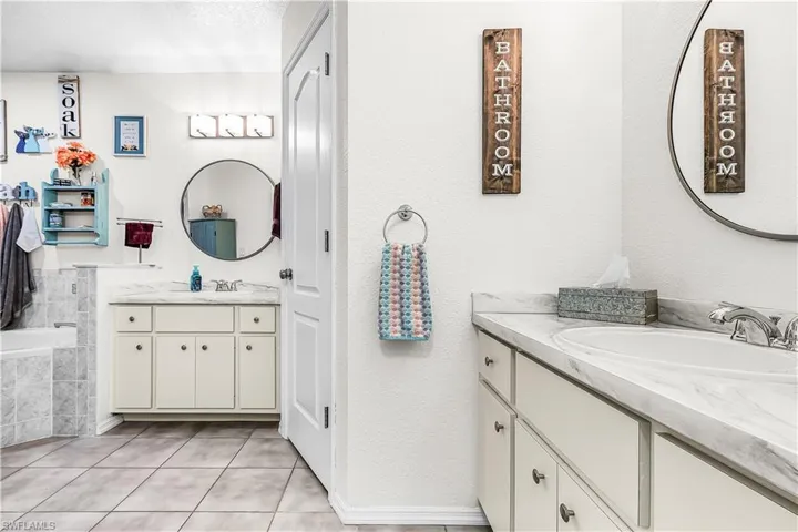 Full bath with two vanities, a textured wall, and light tile patterned flooring