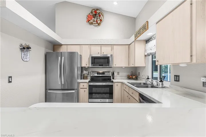 Kitchen featuring light wood finish cabinets, stainless steel appliances, and a textured wall