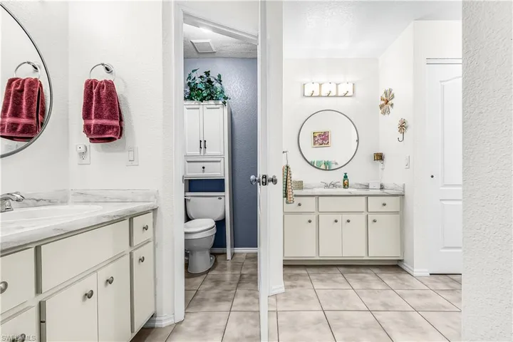 Full bath with a textured wall, two vanities, a textured ceiling, and light tile patterned floors