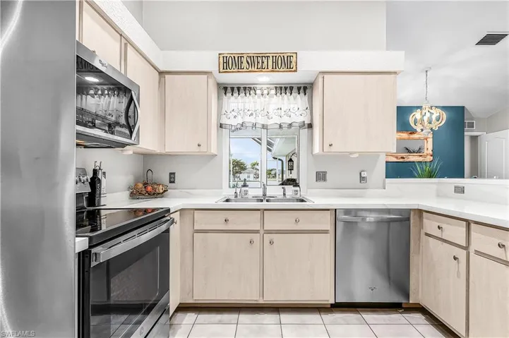 Kitchen featuring light wood finish cabinetry, stainless steel appliances, hanging lights, and light tile patterned floors