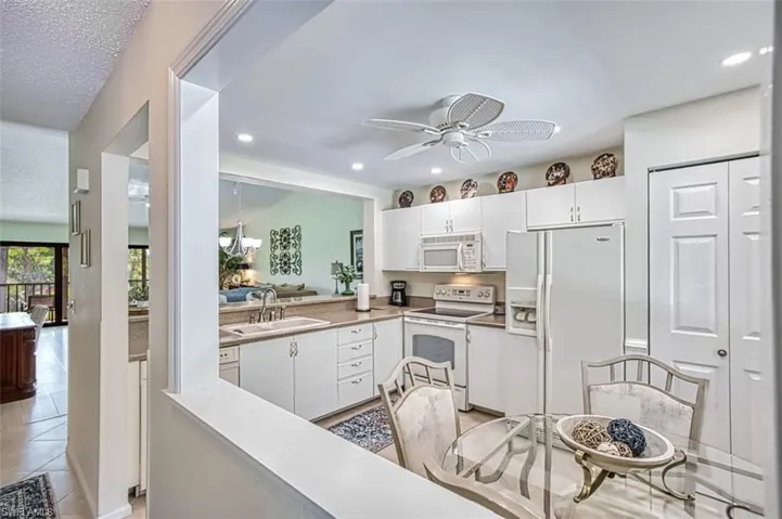 Kitchen featuring white appliances, light tile patterned floors, white cabinets, ceiling fan, and sink