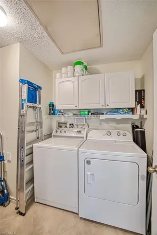 Clothes washing area with washing machine and dryer, a textured ceiling, cabinets, and light tile patterned floors