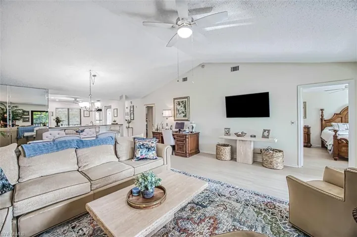 Living room featuring a textured ceiling, light hardwood / wood-style flooring, ceiling fan with notable chandelier, and lofted ceiling