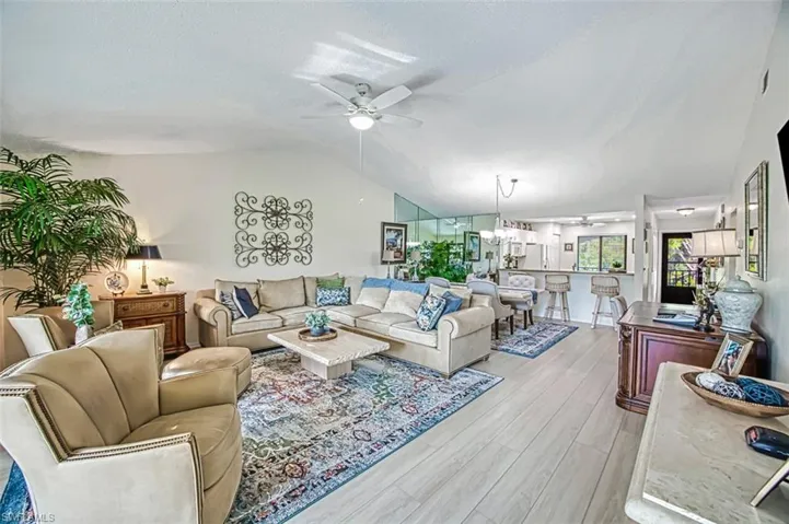 Living room featuring light hardwood / wood-style flooring, ceiling fan with notable chandelier, and lofted ceiling