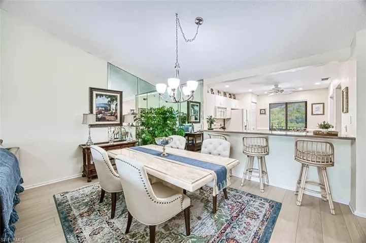 Dining room with light wood-type flooring, ceiling fan with notable chandelier, and vaulted ceiling