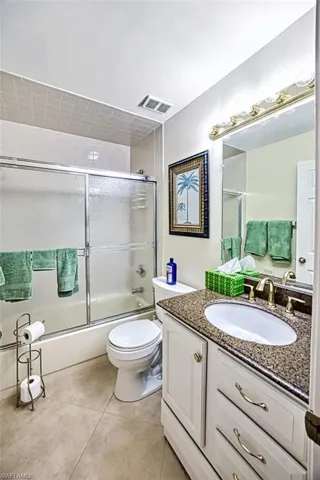 Full bathroom with vanity, combined bath / shower with glass door, tile patterned flooring, and toilet