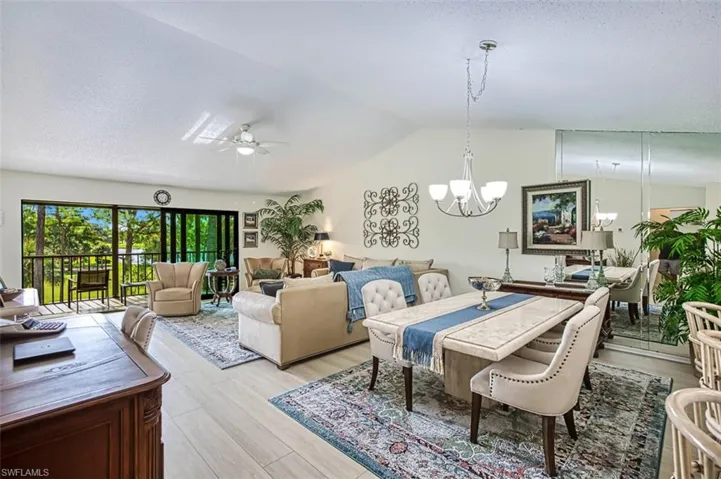 Living room with ceiling fan with notable chandelier, lofted ceiling, light hardwood / wood-style flooring, and a textured ceiling