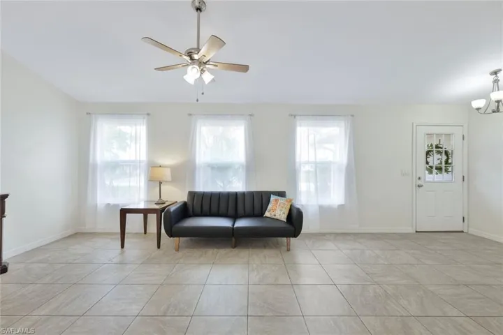 Living area with vaulted ceiling, large square tile flooring throughout, plenty of natural light, and ceiling fan with chandelier in entryway.