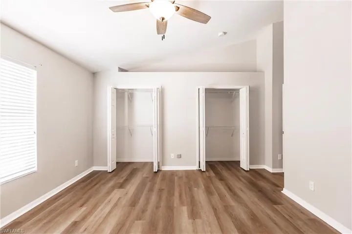 Unfurnished bedroom with hardwood / wood-style floors, multiple closets, ceiling fan, and vaulted ceiling
