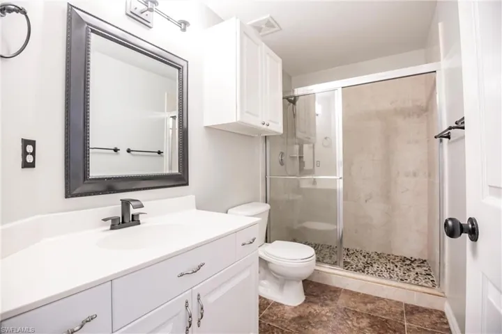Bathroom with toilet, vanity, an enclosed shower, and tile patterned flooring