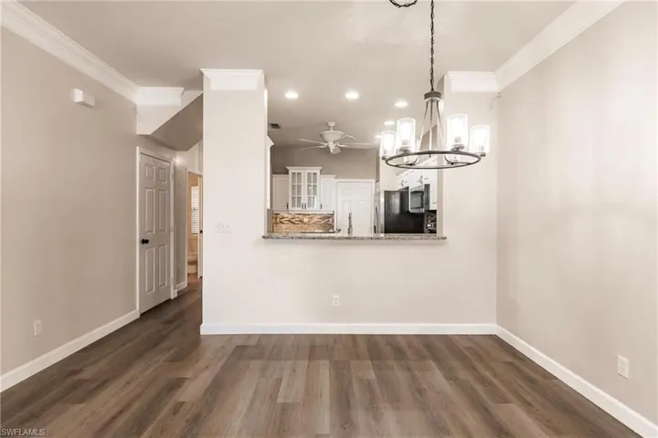 Unfurnished dining area with dark wood-type flooring, ornamental molding, and ceiling fan with notable chandelier