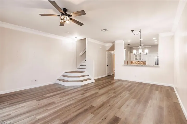 Unfurnished living room with wood-type flooring, ceiling fan with notable chandelier, and crown molding