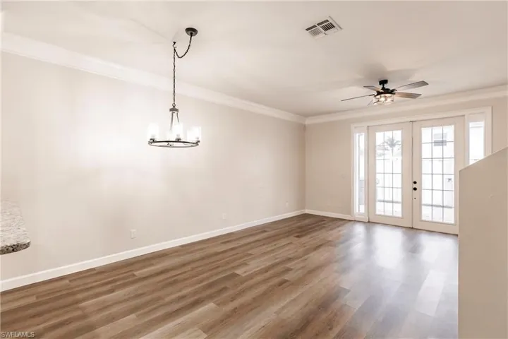 Empty room with french doors, ceiling fan with notable chandelier, dark hardwood / wood-style floors, and crown molding