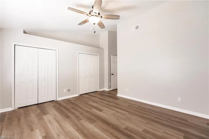 Unfurnished bedroom featuring hardwood / wood-style flooring, ceiling fan, vaulted ceiling, and two closets