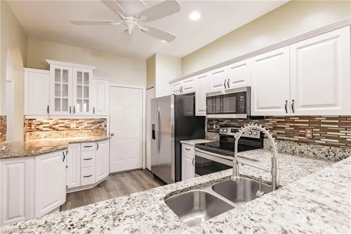 Kitchen with white cabinetry, appliances with stainless steel finishes, light stone counters, and backsplash