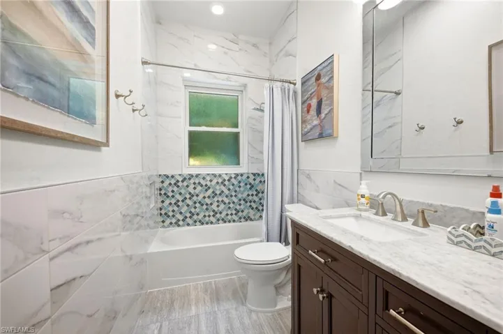 Bathroom featuring a single vanity with a white countertop and dark wood-finish cabinetry, a tub with a shower and subway tile surround, mosaic accent tiling, and a window