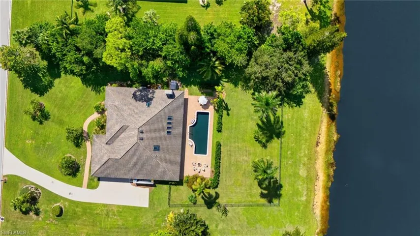 Expansive almost 1 Acre lot property featuring a private swimming pool, fenced backyard, concrete patio, lush green lawn, mature trees, and direct water frontage