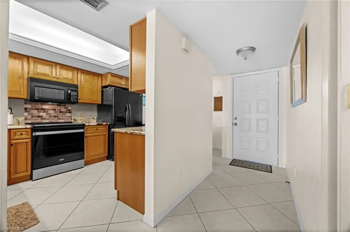Kitchen featuring black appliances, light tile patterned floors, light stone counters, and brown cabinets