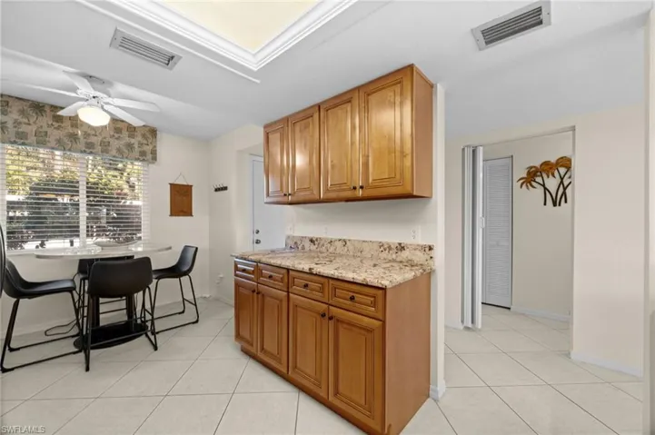 Kitchen with light stone countertops, light tile patterned flooring, brown cabinets, and ceiling fan