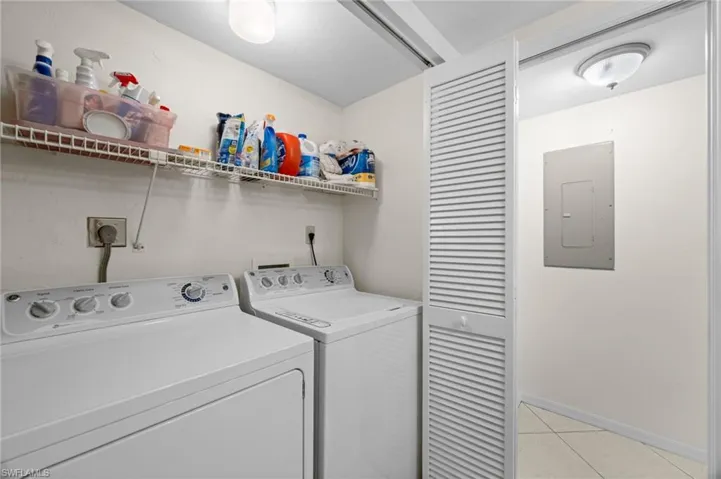 Laundry area featuring electric panel, light tile patterned floors, and washer and clothes dryer
