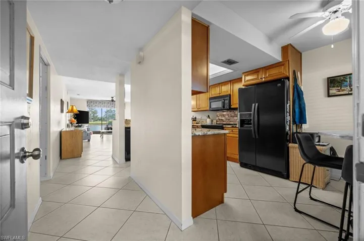 Kitchen with ceiling fan, brown cabinetry, black appliances, and light stone countertops