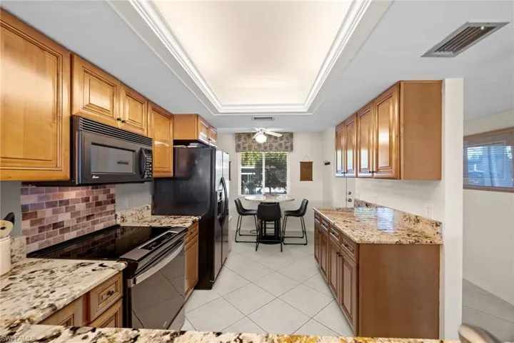 Kitchen with black appliances, light stone countertops, brown cabinetry, a ceiling fan, and a tray ceiling