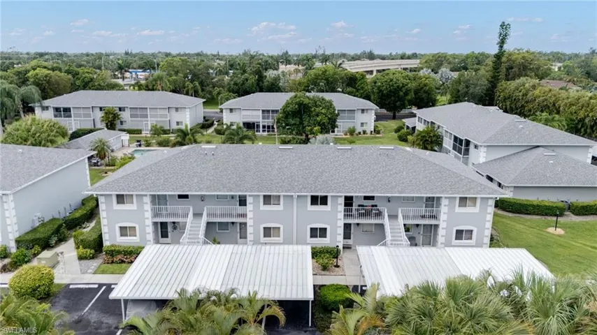 Multi-story residential buildings featuring covered parking, private balconies, and surrounding green spaces with mature trees