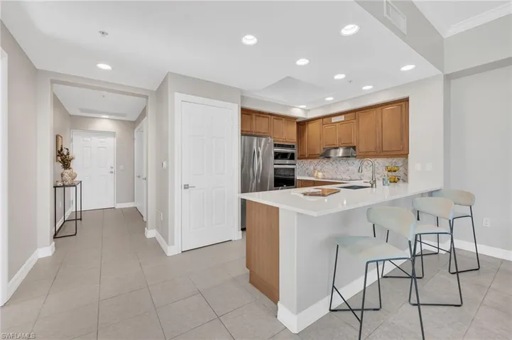 Kitchen featuring wood cabinetry, stainless steel appliances, a tile backsplash, and a breakfast bar with solid surface countertops