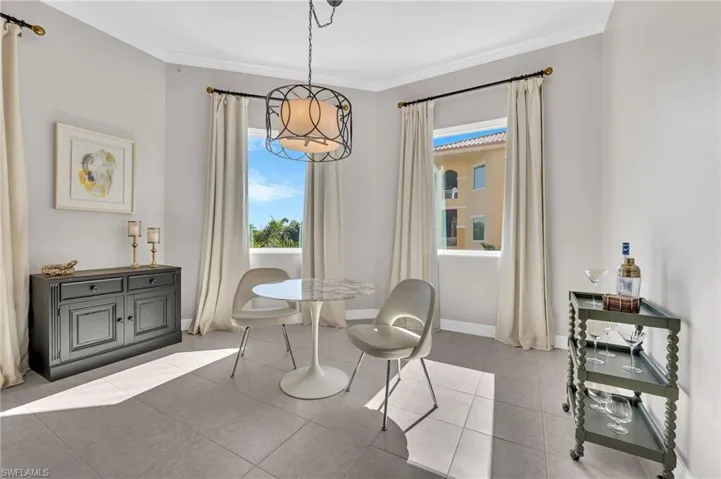 Spacious room featuring light gray tile flooring, crown molding, and two large windows with exterior views