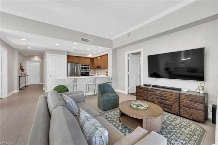 Open-concept living area featuring light-toned tile flooring, recessed lighting, and a kitchen with wood cabinetry and stainless steel appliances