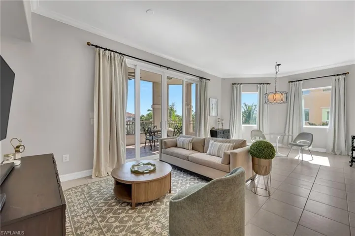 Spacious living area featuring tile flooring, crown molding, and a sliding glass door leading to a balcony