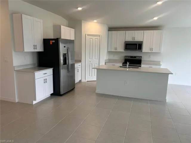 Kitchen with white cabinetry, stainless steel appliances, an island with sink, light tile patterned flooring, and recessed lighting