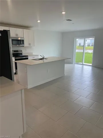 Kitchen featuring appliances with stainless steel finishes, white cabinetry, light tile patterned floors, a center island with sink, and recessed lighting