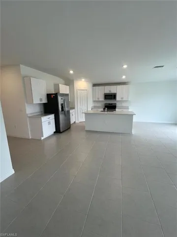Kitchen featuring white cabinets, light countertops, appliances with stainless steel finishes, open floor plan, and light tile patterned floors