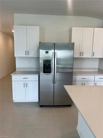 Kitchen with white cabinets, stainless steel refrigerator with ice dispenser, light tile patterned floors, and light stone counters