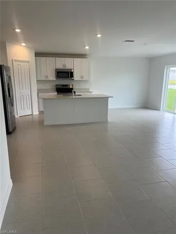 Kitchen featuring appliances with stainless steel finishes, an island with sink, white cabinets, light tile patterned floors, and open floor plan
