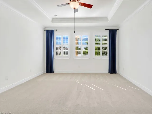 Primary Bedroom With Plantation Shutters On The Wall Of Windows Viewing The Lake & Tray Ceiling With Crown Molding
