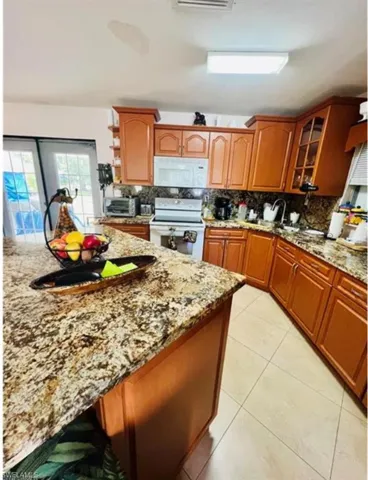 Kitchen with backsplash, white appliances, light tile patterned floors, light stone countertops, and brown cabinetry