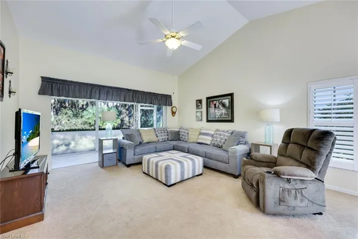 Carpeted living area with high vaulted ceiling, a wealth of natural light, and a ceiling fan