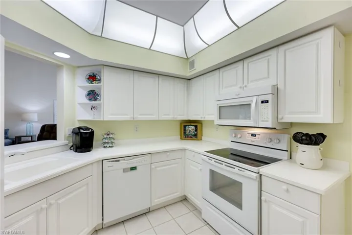 Kitchen with white appliances, light tile patterned floors, visible vents, white cabinetry, and a sink