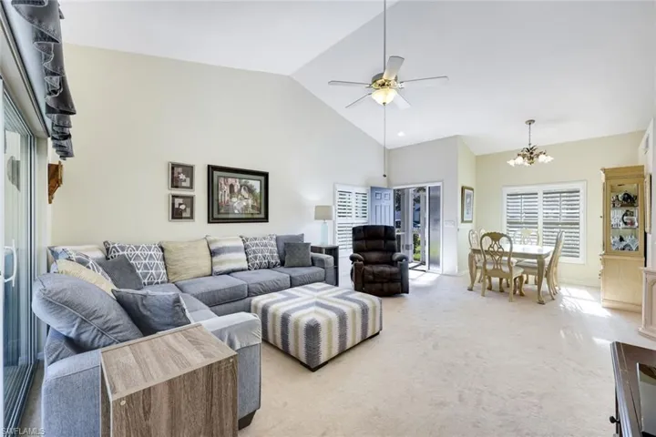 Living room featuring high vaulted ceiling, light colored carpet, and ceiling fan with notable chandelier