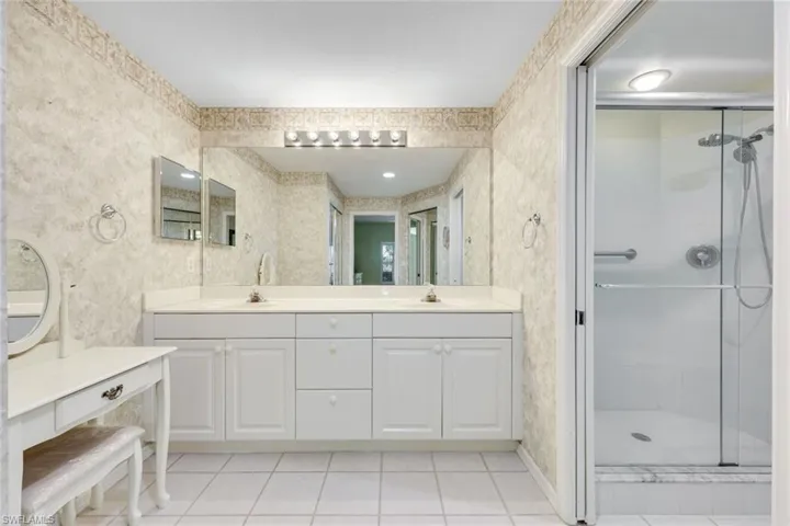 Bathroom with wallpapered walls, tile patterned flooring, a sink, and a stall shower