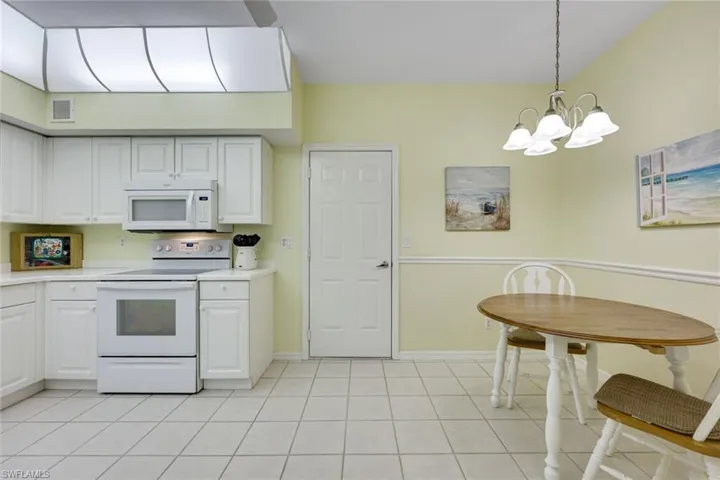 Kitchen with light tile patterned floors, white appliances, white cabinets, and light countertops