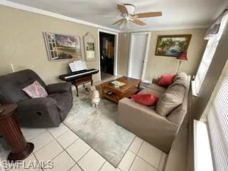 Living room with light tile patterned floors, ornamental molding, and ceiling fan