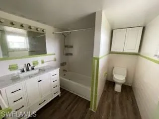 Full bathroom featuring hardwood / wood-style flooring, tiled shower / bath, vanity, and toilet