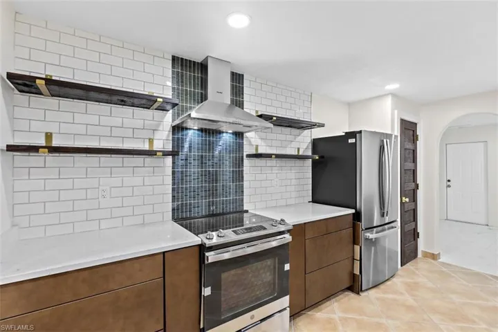 Kitchen with light tile patterned flooring, electric range oven, decorative backsplash, and wall chimney range hood